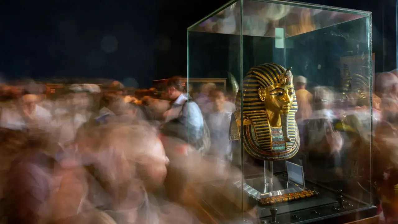 Goldene Maske des Pharao Tutanchamun in einer Vitrine, umgeben von verschwommenen Besuchern.