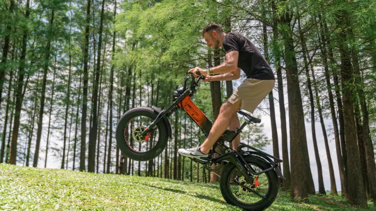 Un homme fait du vélo électrique sur une pente herbeuse, le pneu avant décollé du sol. Ce vélo électrique pour forte pente est idéal pour les terrains difficiles.