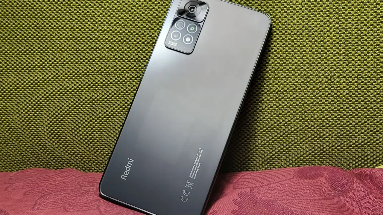 Elegancki, szary Redmi Note 11 Pro 5G Plus z aparatem 108MP na tle zielonej i bordowej tkaniny.