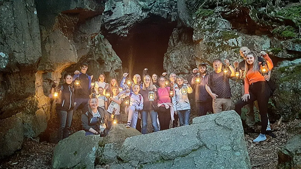 Grupa ludzi z latarniami przy skalnej grocie, odkrywająca tajemnice szlaku walońskiego.