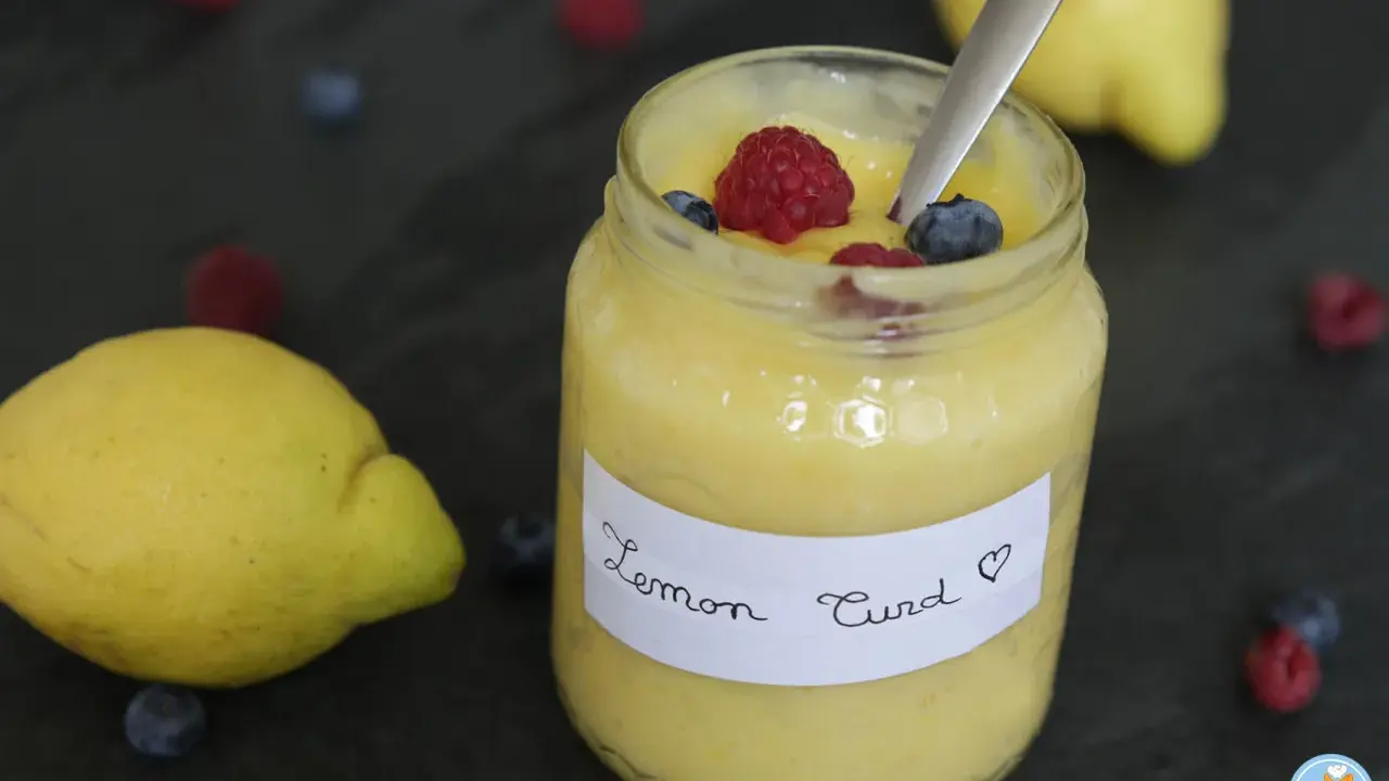 Un pot de lemon curd maison, garni de framboises et myrtilles, avec des citrons frais et des baies éparpillés.