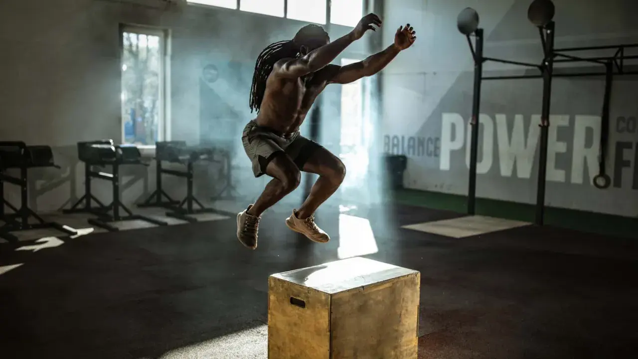 Mann mit Dreadlocks macht explosive Box Jumps in einem nebeligen Fitnessstudio.