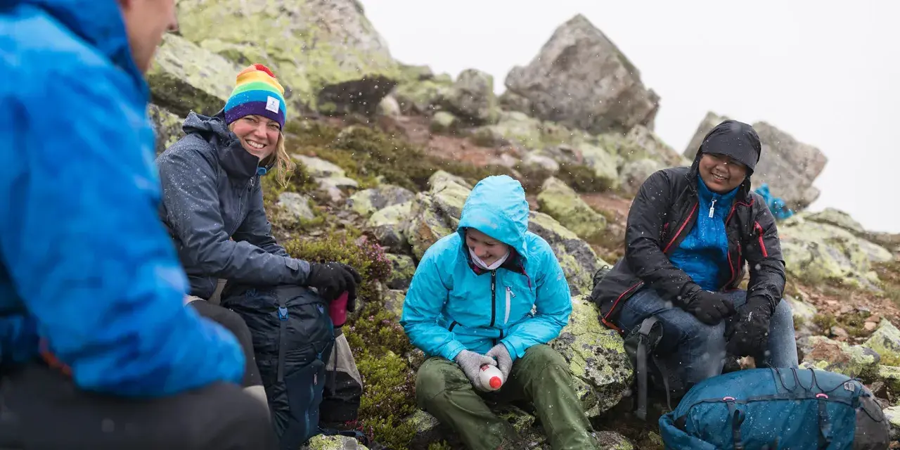 Vänner vilar på berg i snöfall, deras impregnerade jackor håller dem torra.