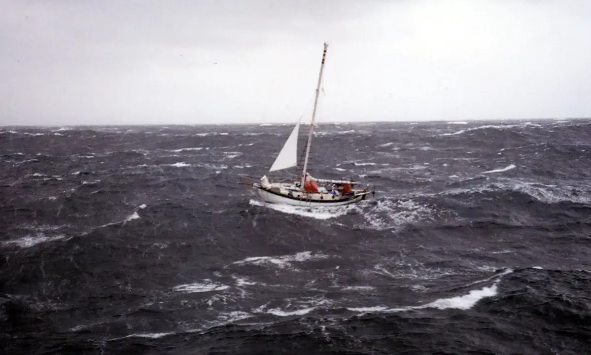Un voilier affronte une mer agitée, sa voile blanche tendue. La mise à la cape est une manœuvre de survie face aux éléments déchaînés.