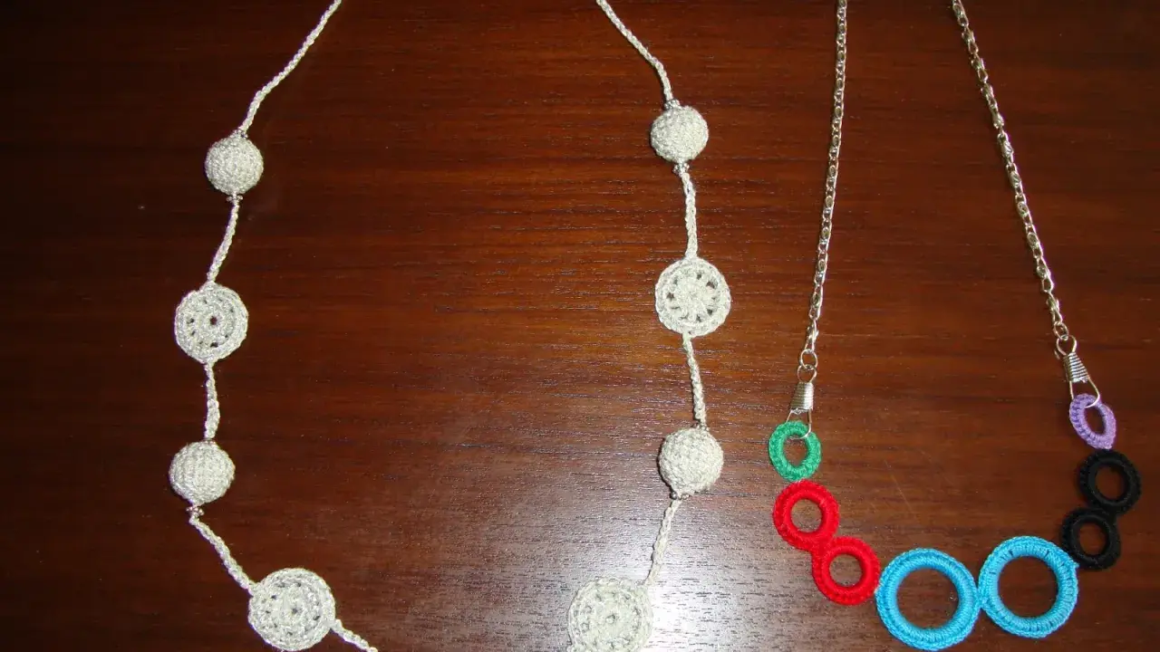 Dos collares de ganchillo y abalorios: uno blanco con esferas y círculos calados, y otro con cadena plateada y aros de colores.
