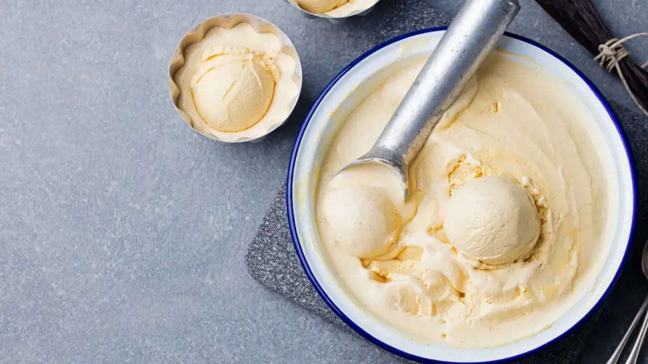 Glace vanille sorbetière crémeuse, servie dans un bol avec une cuillère à glace. Des gousses de vanille sont disposées à côté.