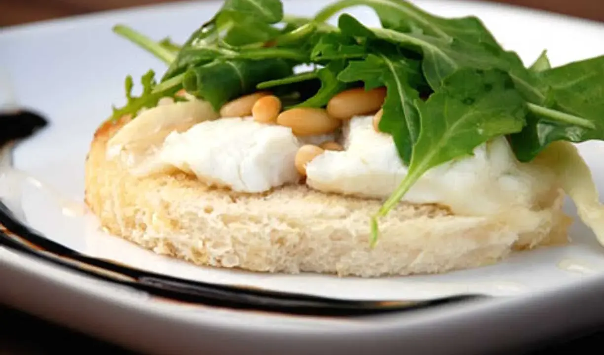 En bit rostat bröd med smält **chevre chaud**, pinjenötter och ruccola. En läcker förrätt.