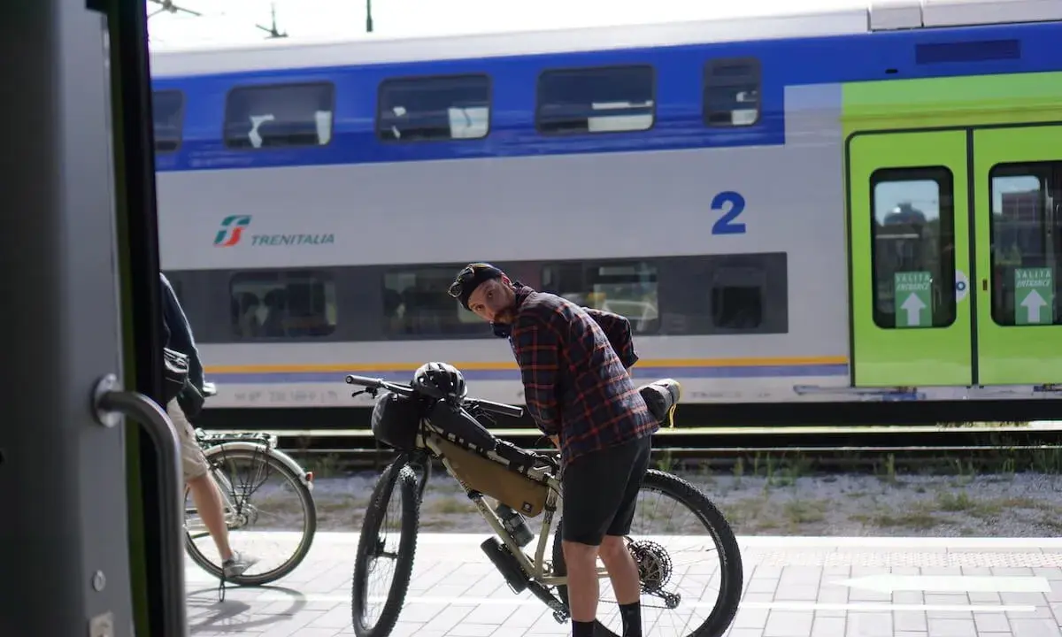 Ciclista con bici da gravel alla stazione, pronto per il viaggio da Rimini a Bellaria. Il treno Trenitalia è sullo sfondo.