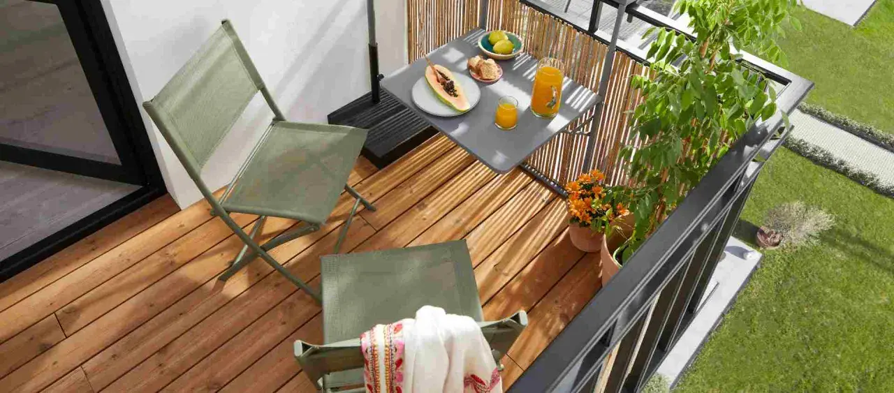 Idéal pour aménager un petit balcon en longueur : deux chaises pliantes vertes, une table avec fruits et jus, et des plantes.