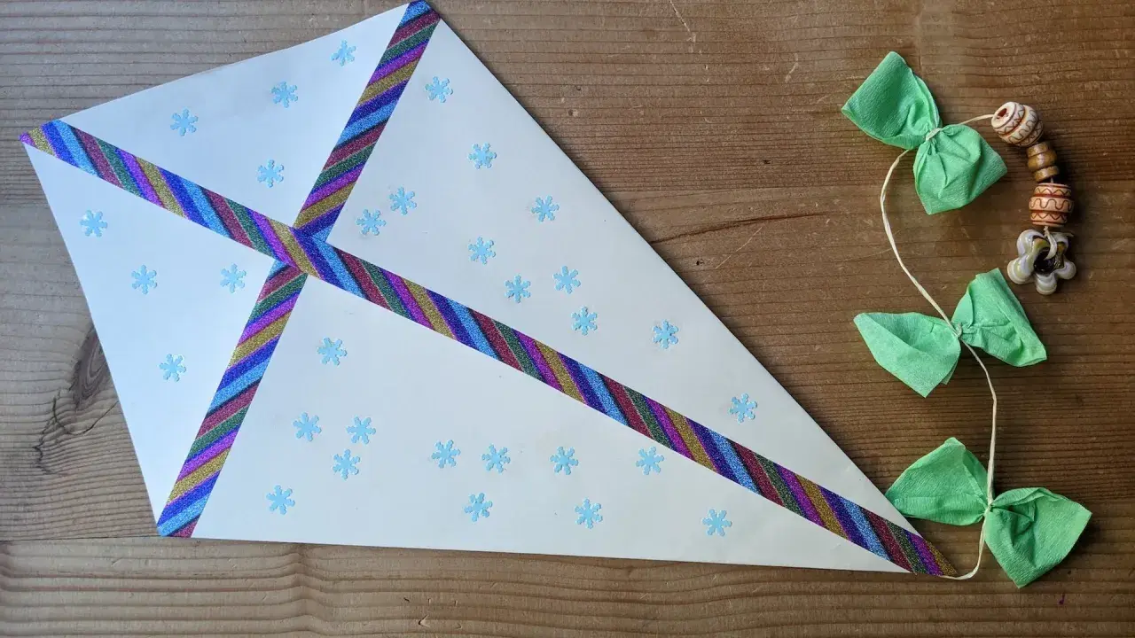 Ein selbstgebastelter Drachen mit Schneeflocken und bunten Bändern, perfekt für basteln mit Kindern ab 7 Jahre. Daneben eine Schnur mit grünen Schleifen und Holzperlen.
