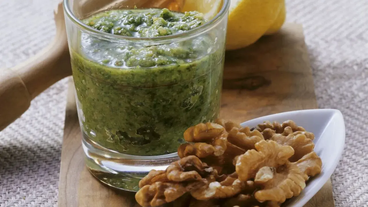 Frisches Petersilienpesto im Glas, daneben Walnüsse und eine Zitronenhälfte. Perfekt für Petersilie Rezepte.