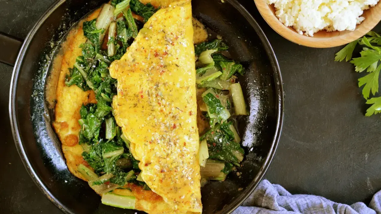 Omlet z serka wiejskiego z zielonymi warzywami na patelni. Obok miseczka z serkiem i natka pietruszki.