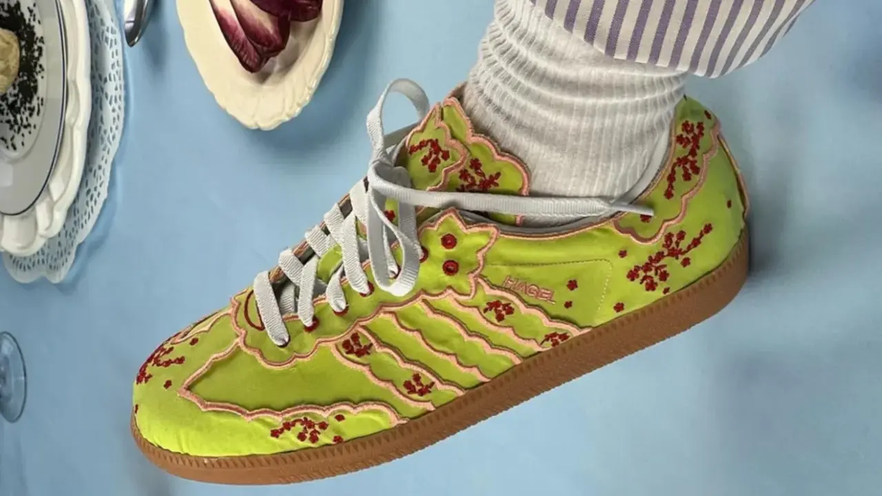 Jaskrawozielone buty Adidas z haftowanymi kwiatami wiśni i różowymi lamówkami, prawdopodobnie najdroższe buty Adidas, prezentowane na błękitnym tle.