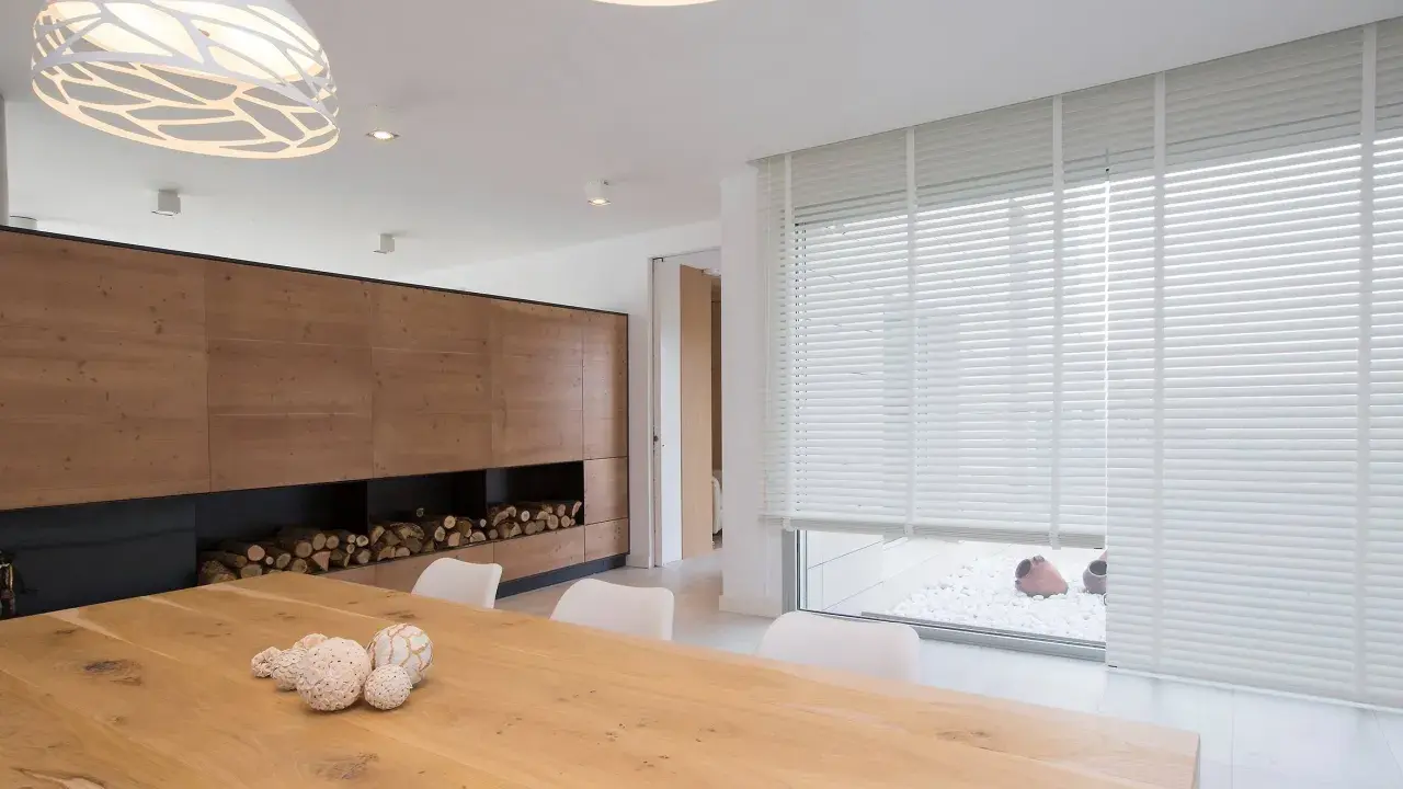 Un salon moderne avec un grand mur en bois, une table en bois et un type de store vénitien blanc qui habille une large fenêtre.