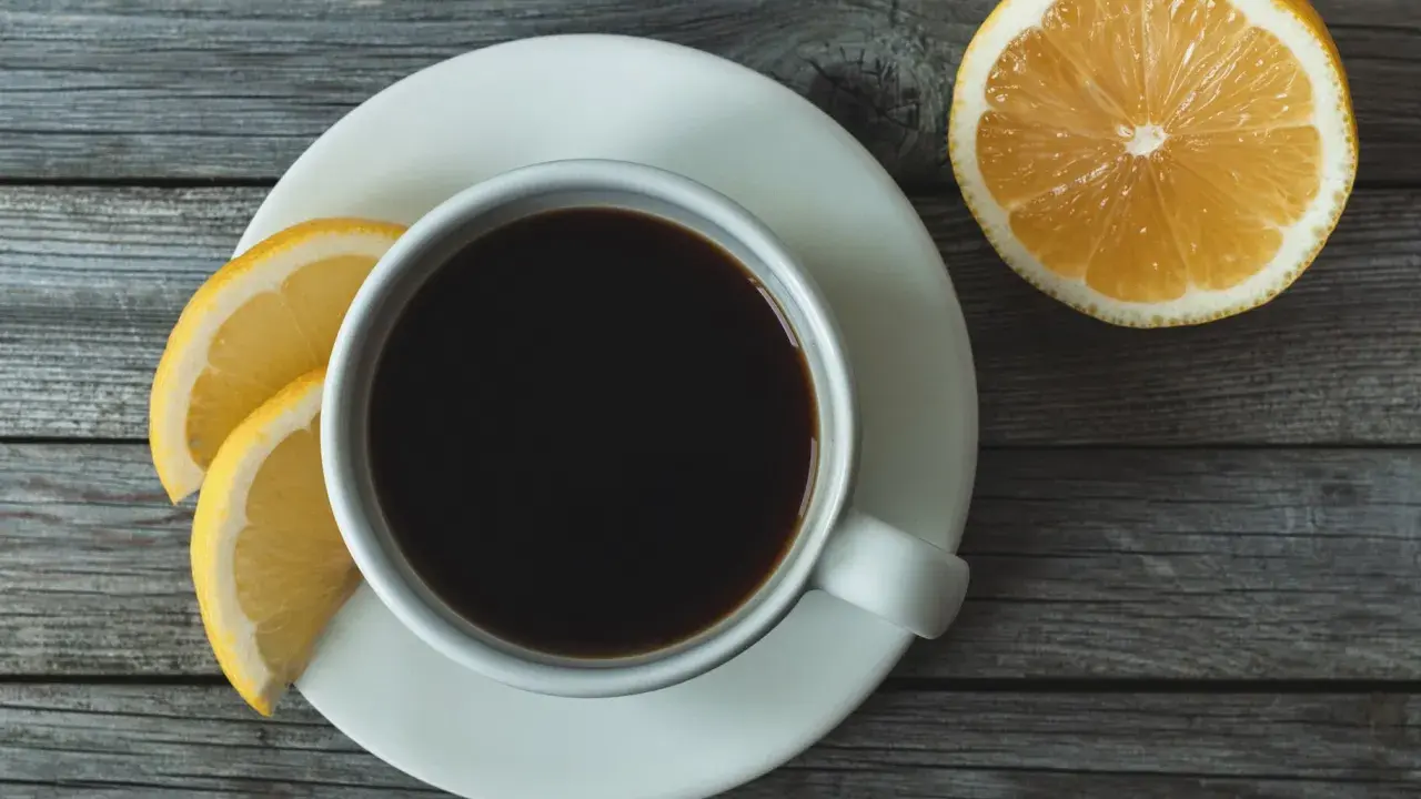 Eine Tasse schwarzer Kaffee mit Zitrone und Zitronenscheiben auf einem Holztisch.