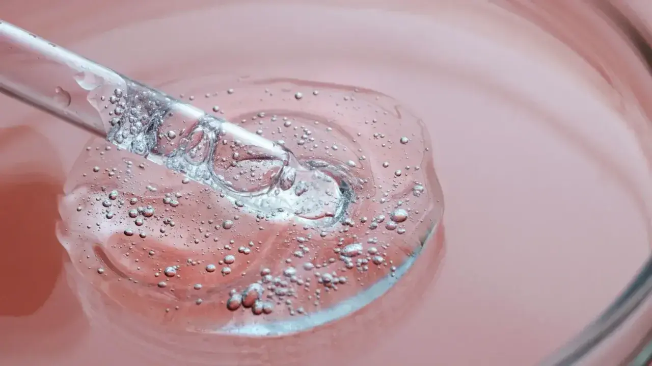 Goutte d'un sérum transparent avec des bulles, sur fond rose. C'est une illustration de ce que sont les peptides, des éléments clés pour la peau.