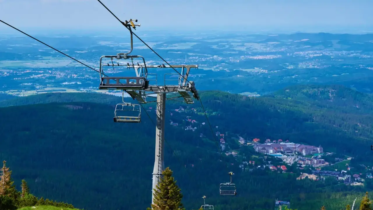 Karpacz i Szklarska Poręba z lotu ptaka. Kolejka linowa wznosi się nad zielonymi lasami i zabudowaniami.