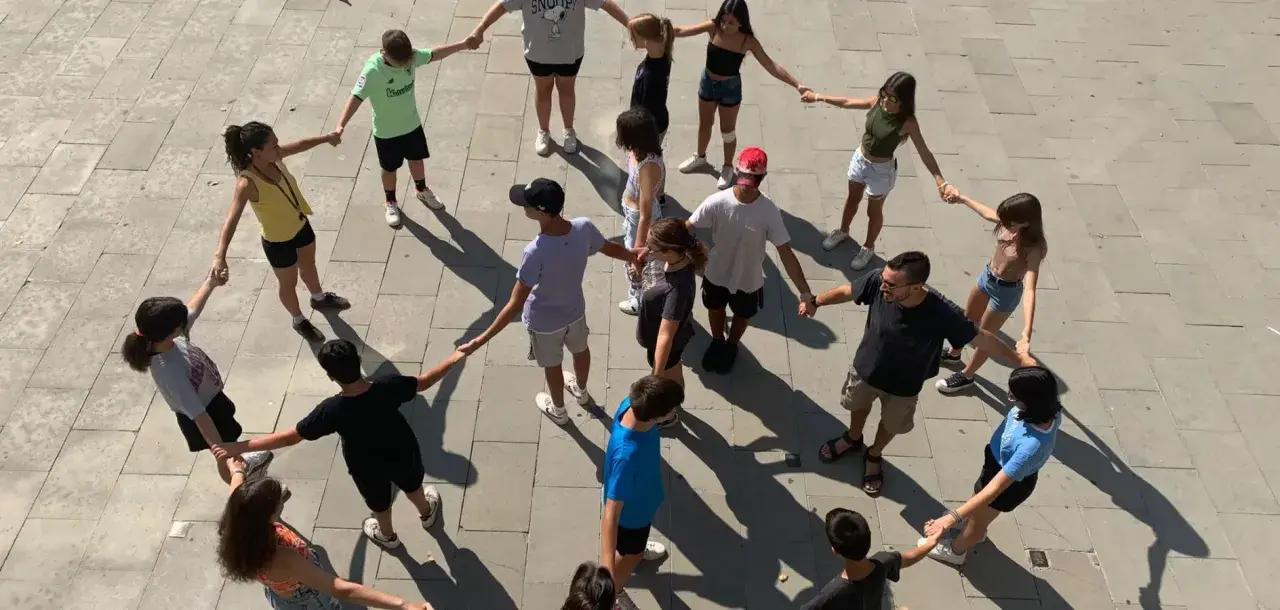 Un grupo de adolescentes participa en juegos cooperativos, tomados de la mano en un círculo en el exterior.