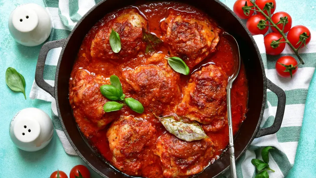 Un saporito pollo in umido, cotto lentamente in una ricca salsa di pomodoro, guarnito con basilico fresco e alloro.