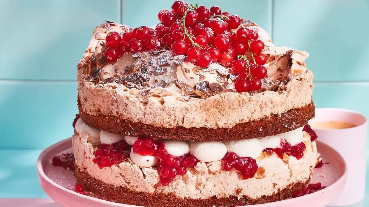 Ein zweistöckiger Johannisbeerkuchen mit Baiser, Sahne und roten Johannisbeeren, bestäubt mit Puderzucker und Mandelsplittern.