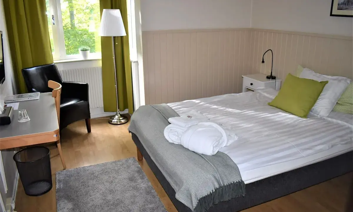 Ett mysigt rum på Wendelsbergs Hotell & Vandrarhem med en bekväm säng, fåtölj och skrivbord.