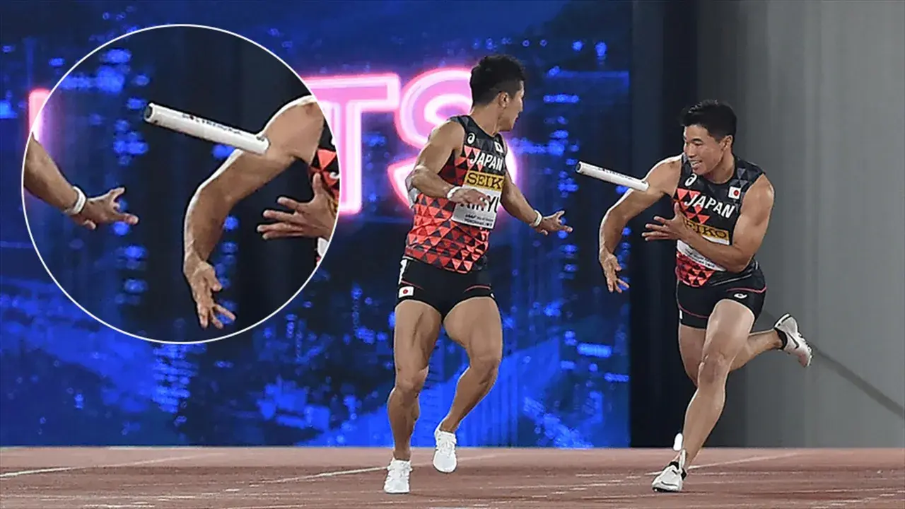 Dwóch lekkoatletów z Japonii w trakcie biegu z pałeczką. Jeden z nich biegnie, drugi wyciąga rękę po pałeczkę.