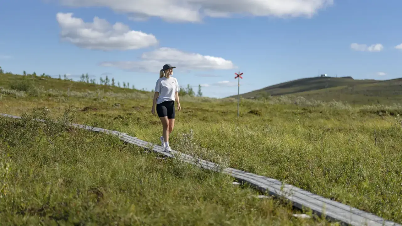 Kvinna vandrar på spång i Gällivare, Sverige. En röd markering syns i bakgrunden.