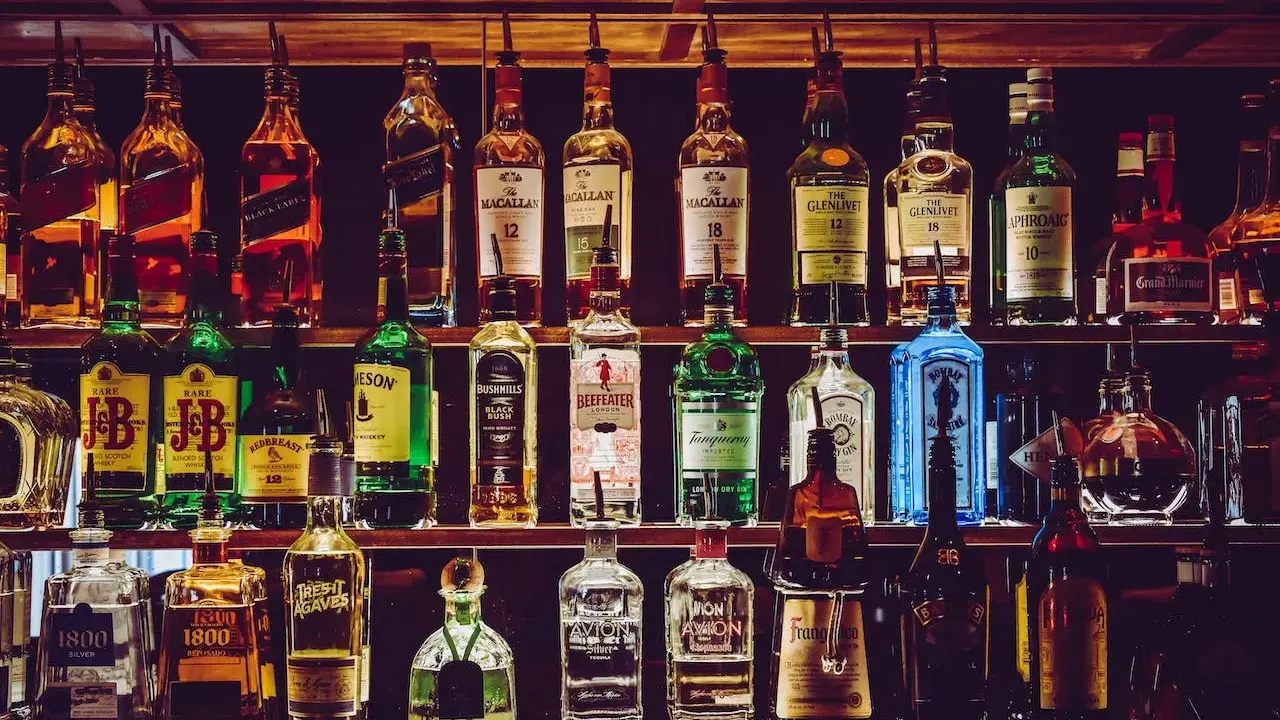 Rzędy butelek alkoholi, w tym whisky, ginu i likierów, na półkach baru.