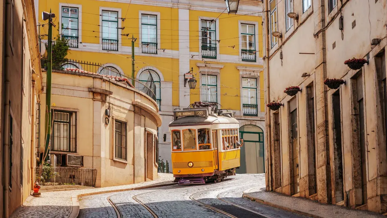 Gelbe Straßenbahn fährt durch enge Gassen Lissabons. Perfekt für angenehme Portugal Temperaturen im Mai.