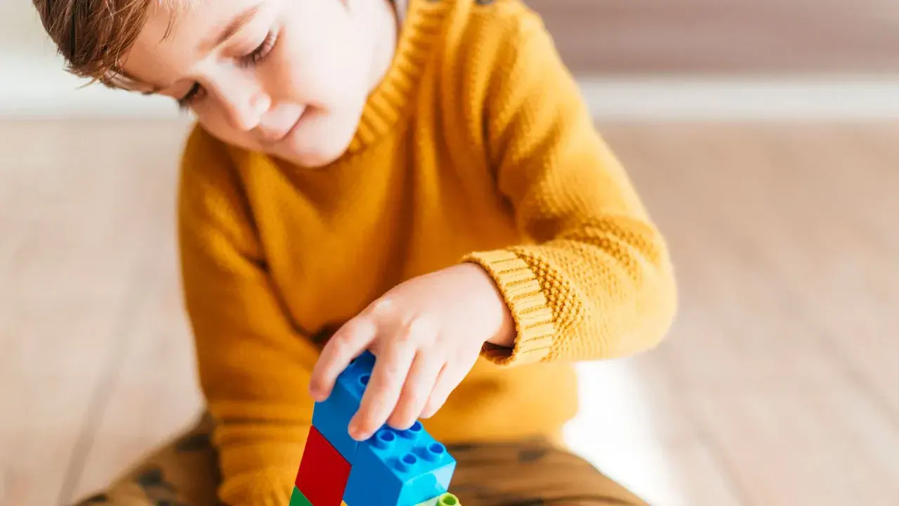 Niño concentrado jugando con bloques de construcción. Un ejemplo de cómo el juego puede ayudar a superar un retraso madurativo y TDAH.