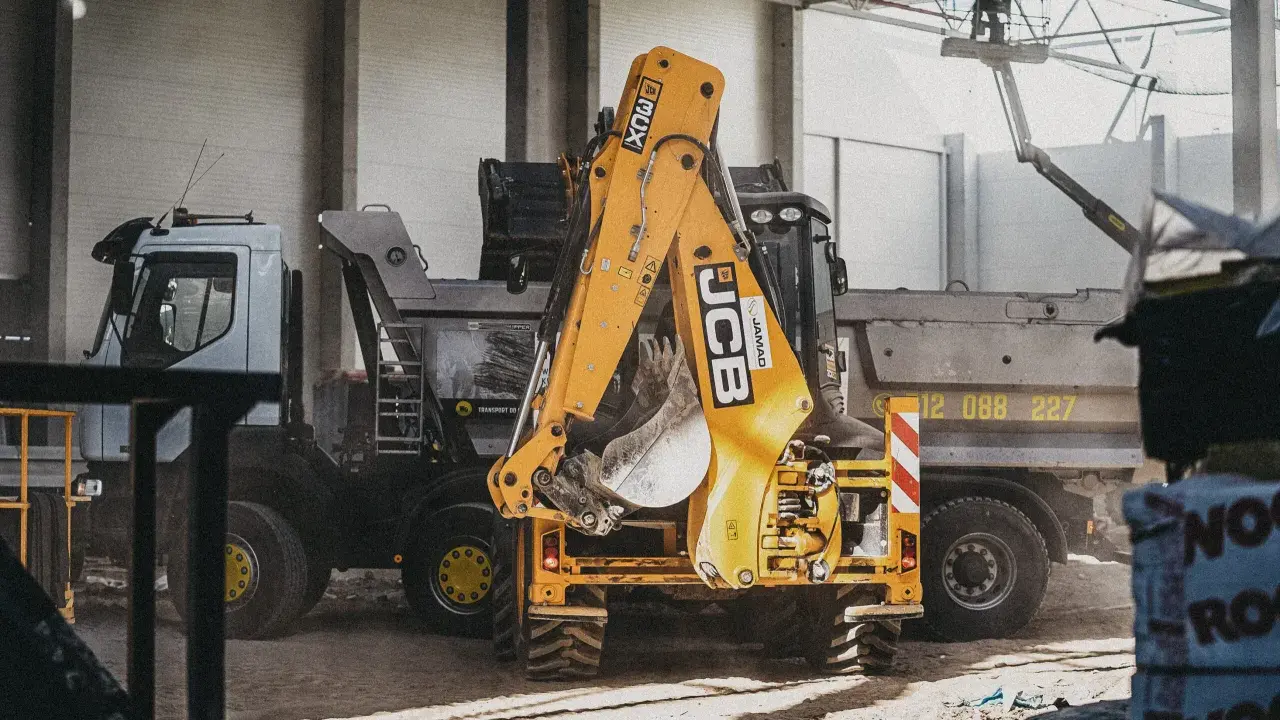 Żółty koparko-ładowarka JCB i ciężarówka na placu budowy.