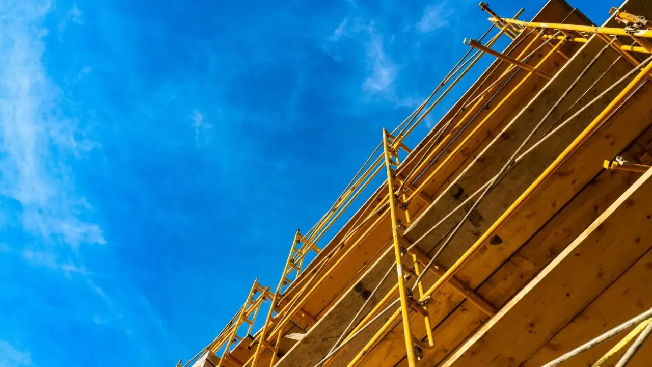 Estructura amarilla de madera y metal, que es una cimbra, contra un cielo azul con nubes finas.