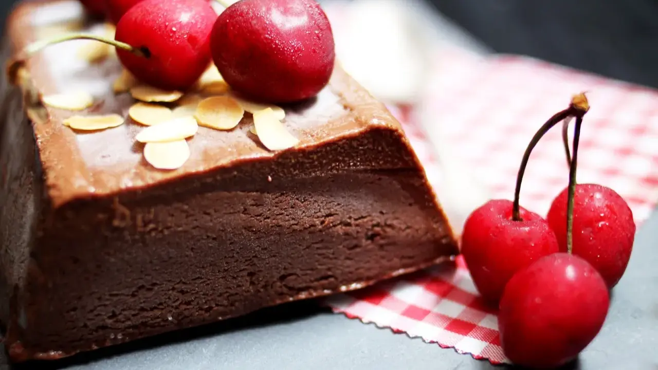 Une délicieuse marquise au chocolat, garnie de cerises fraîches et d'amandes effilées, prête à être dégustée.