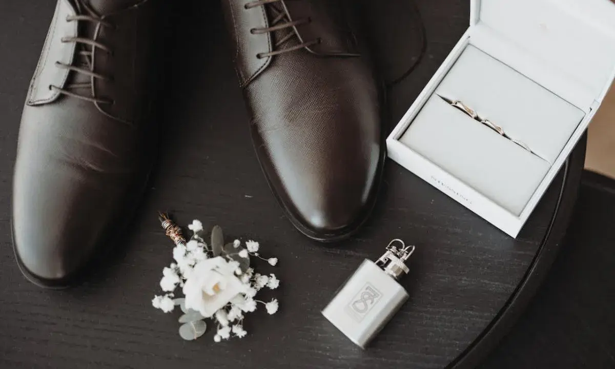 Eleganckie brązowe buty męskie, butonierka, pierścionki w pudełku i piersiówka.
