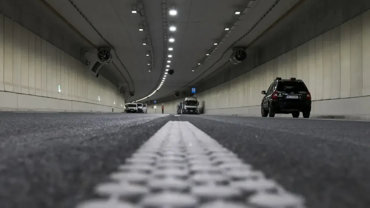 Wnętrze tunelu z samochodami i ciężarówką. Widać wyraźnie jaki odstep w tunelu między pojazdami, oświetlenie i wentylatory.