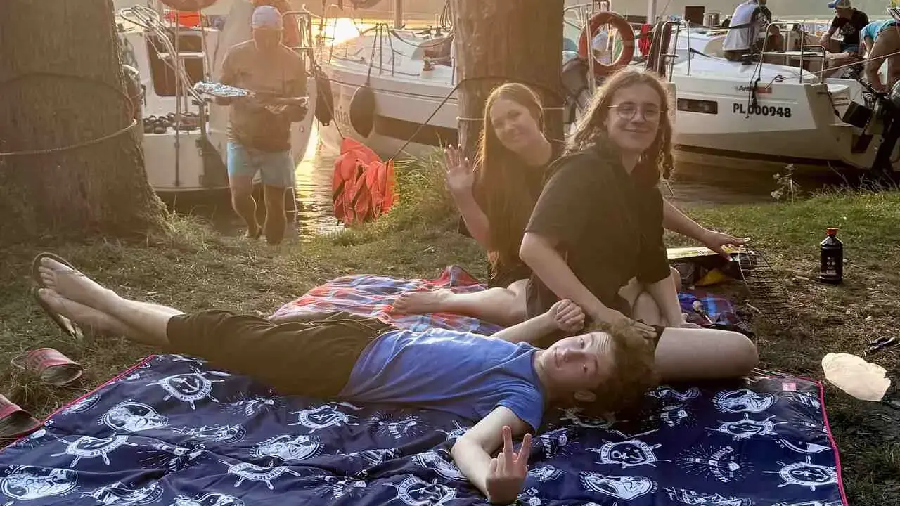 Relaks na kocyku z morskim motywem podczas długiego weekendu czerwiec 2026. W tle łodzie i zachód słońca.