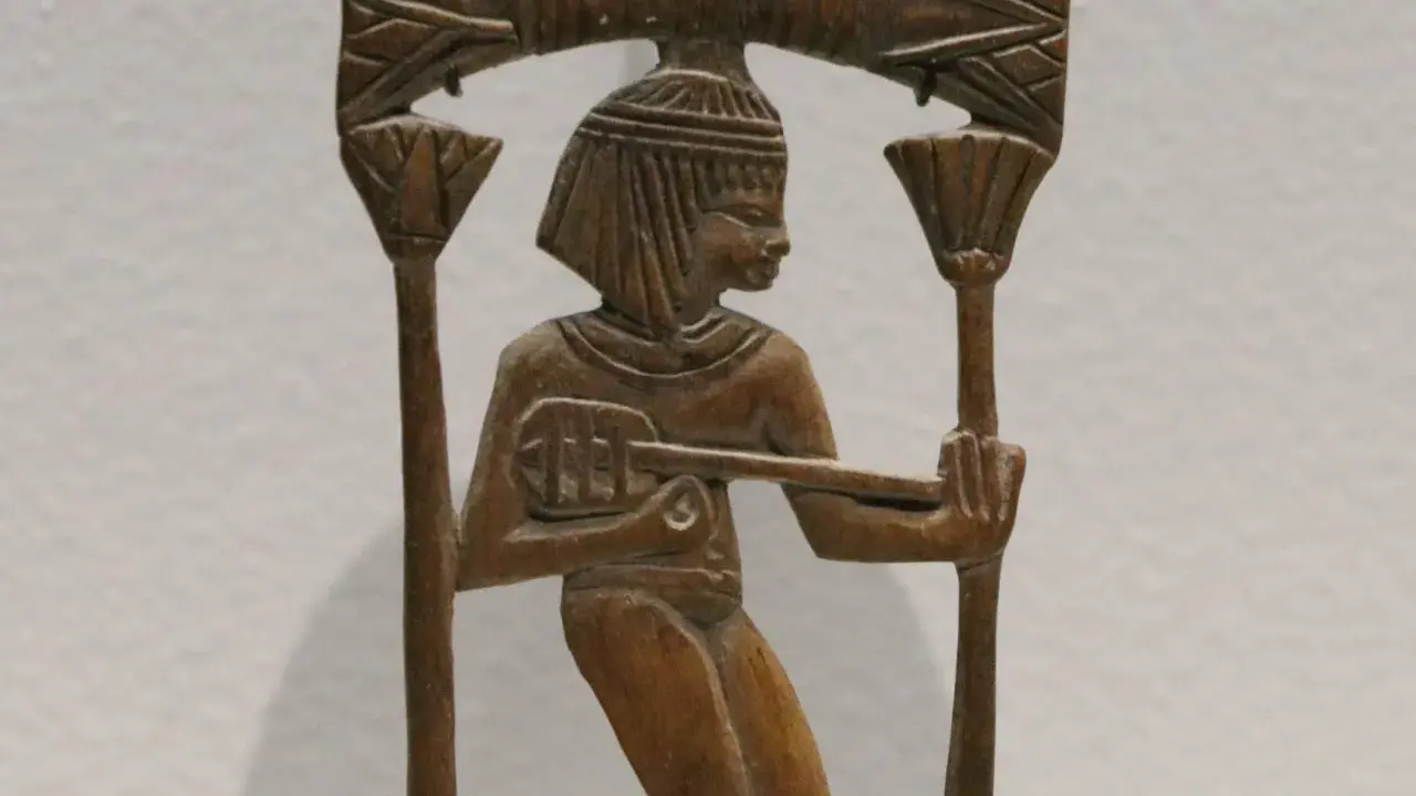 Sculpture en bois d'un musicien égyptien jouant d'un instrument ancien, ornée de motifs floraux.
