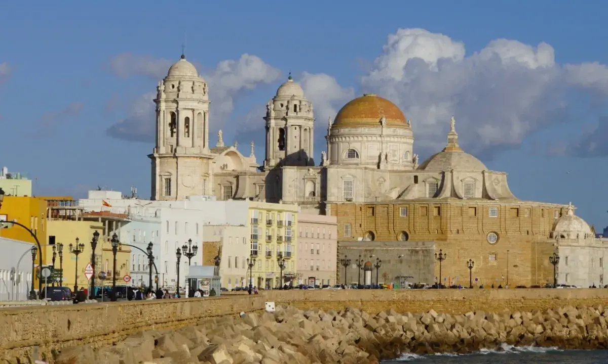 Die Kathedrale von Cadiz, ein majestätisches Bauwerk mit goldenen Kuppeln, ragt über bunte Häuser am Meer auf.