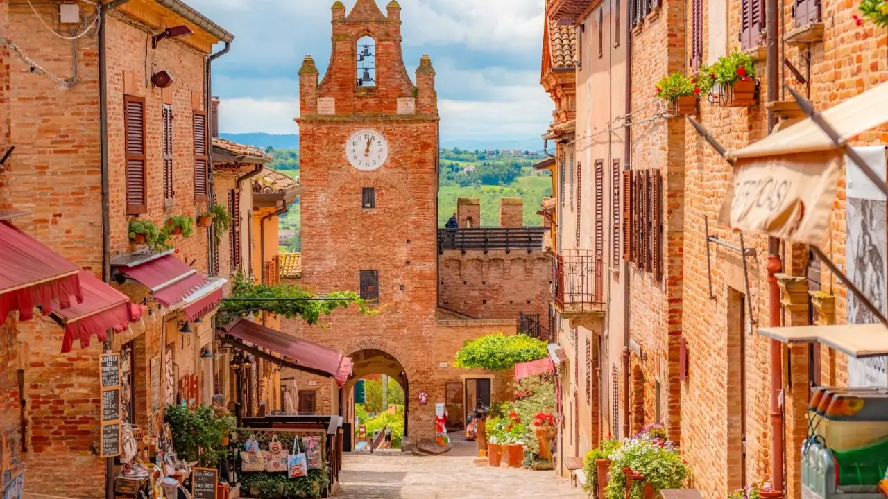 Un vicolo pittoresco a Gradara e dintorni, con case in mattoni, negozietti e un'antica torre dell'orologio.