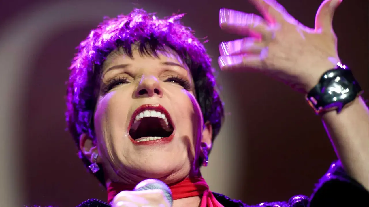 Liza Minnelli, en ikonisk artist, sjunger med passion på scenen, hennes ansikte upplyst av lila ljus.