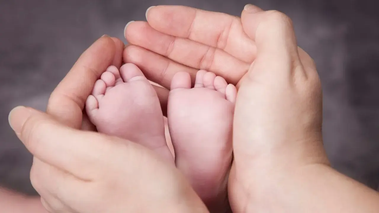 Manos adultas sostienen delicadamente los pies de un bebé. A partir de la semana 37, un bebé puede nacer.