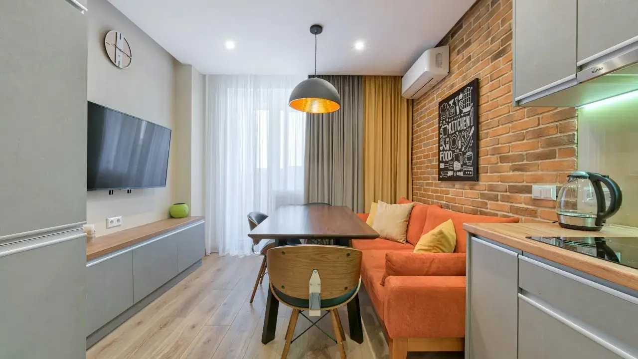 Idée pour aménager salon salle à manger 15m2 : canapé orange, table en bois, mur brique, cuisine moderne.