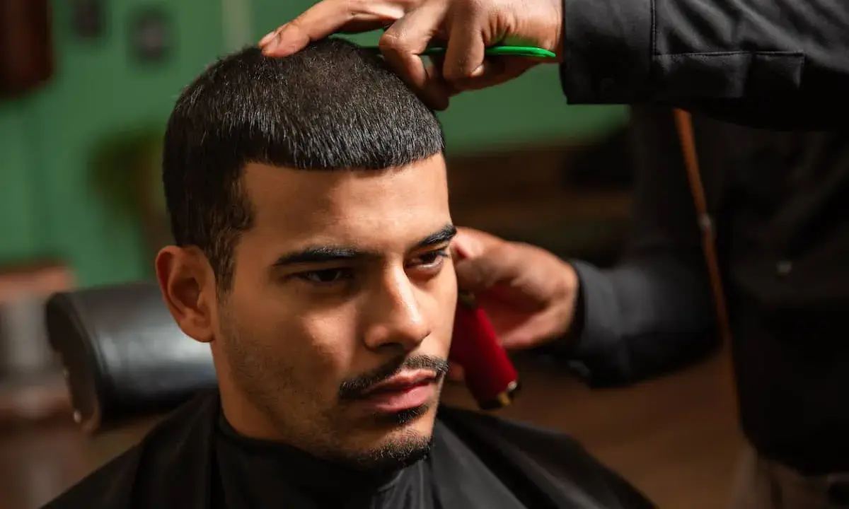 Mann mit Buzz Cut beim Friseur. Hände trimmen das Haar mit einer Schere und einem Trimmer.