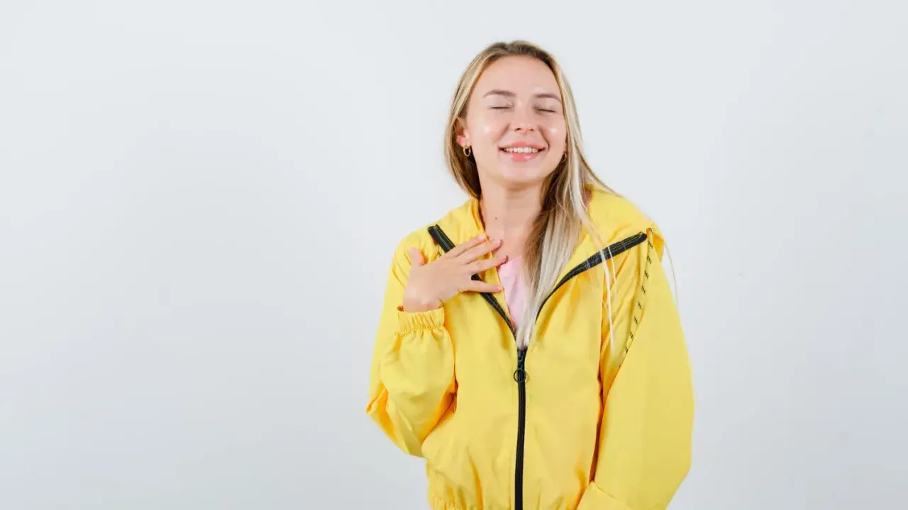 Uśmiechnięta blondynka w żółtej kurtce softshellowej, która przypomina jej, jak prać softshell, by zachować jego właściwości.
