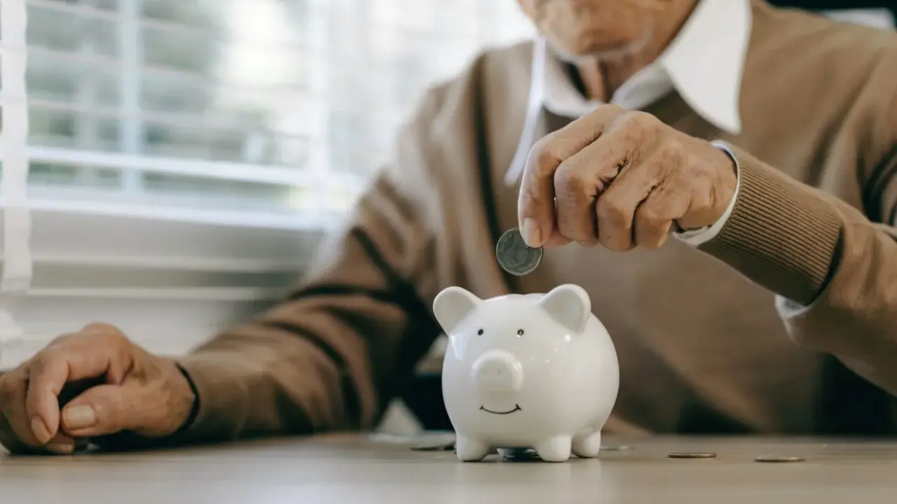 Un anciano deposita una moneda en una hucha, preparándose para la jubilación obligatoria.