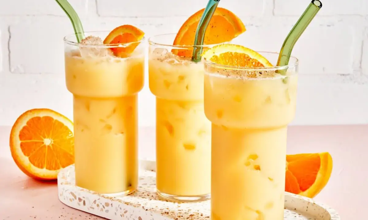 Drei cremige, eisgekühlte Painkiller Cocktails mit Orangenscheiben und grünen Strohhalmen auf einem Terrazzo-Tablett.