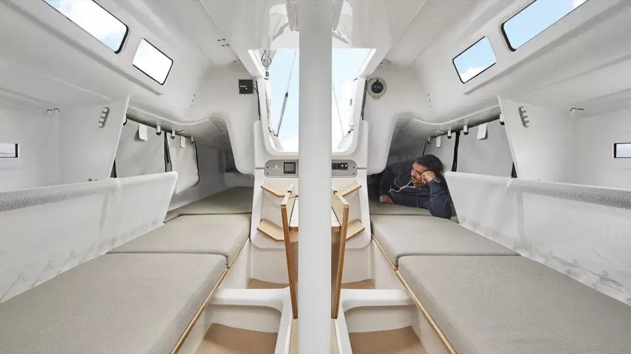 L'intérieur du voilier, premier 27, offre des couchettes confortables et un espace de vie lumineux. Un homme se repose, profitant du calme.