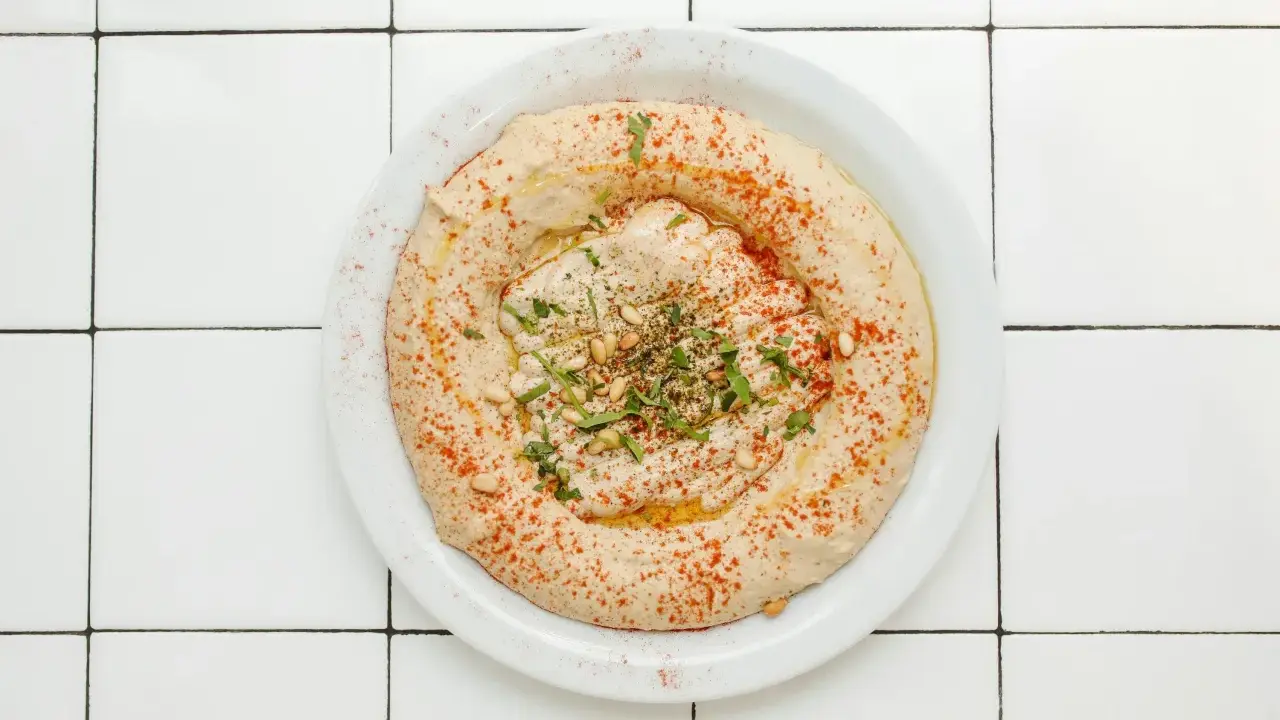 Cremiger Hummus-Dip mit Paprikapulver, Pinienkernen und Petersilie auf einem Teller, bereit zum Dippen.