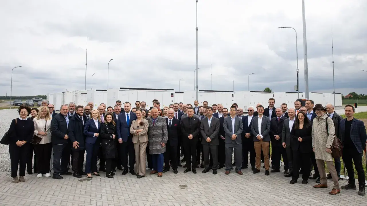 Grupa osób przed bateryjnymi magazynami energii, symbolizującymi rozwój polskiego stowarzyszenia magazynowania energii.