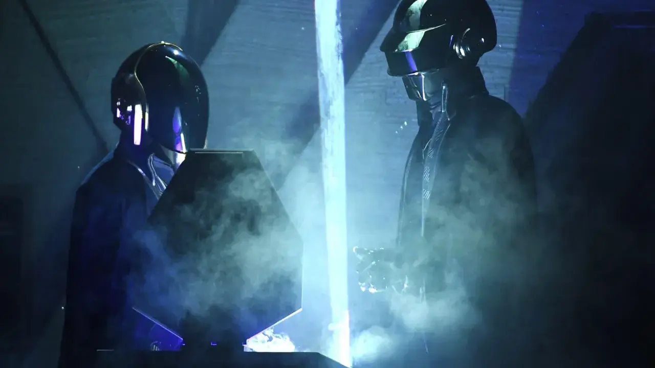 Medlemmar av Daft Punk i sina ikoniska hjälmar, omgivna av rök och blått ljus på scenen.